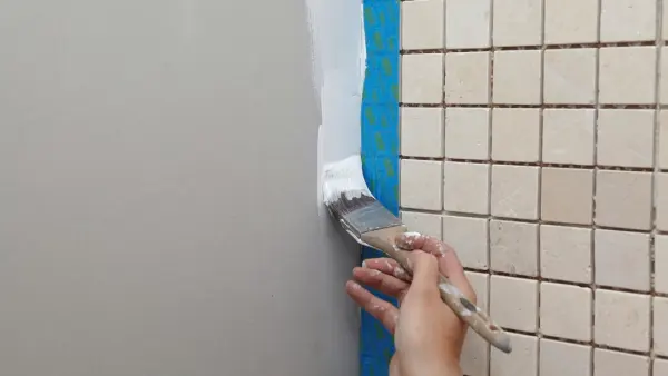 Bàn tay đang sơn cạnh tường gạch men với băng keo che chắn.