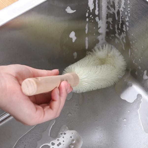 Bàn tay cầm cọ rửa chén bát trên bồn rửa nhà bếp có bọt xà phòng.