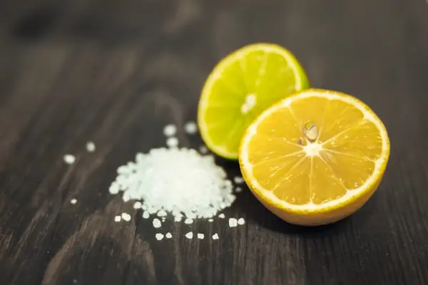 Đĩa đựng chanh cắt đôi và muối rắc trên bàn gỗ.