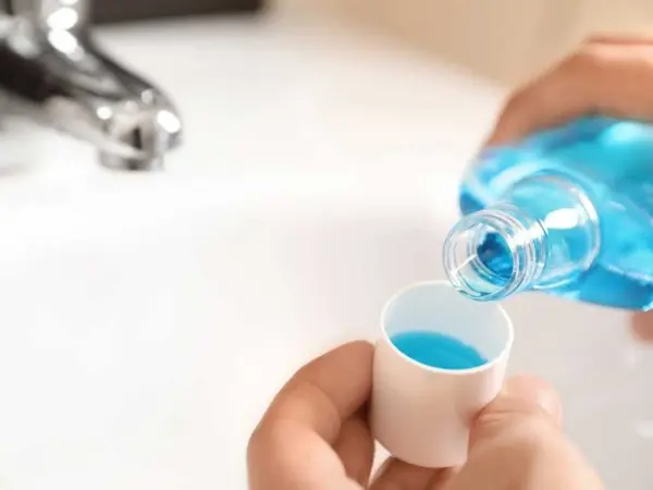 Đang đổ nước rửa bát màu xanh từ chai vào cốc đong.