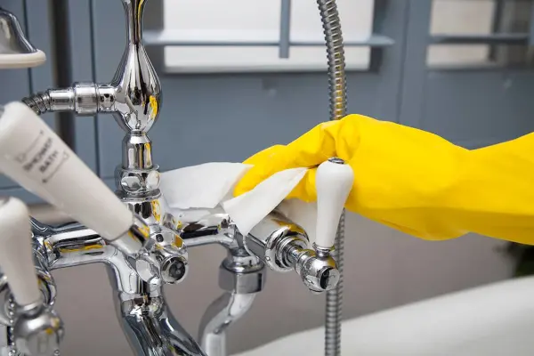 Tay cầm mặc găng tay màu vàng đang lau vòi sen bằng khăn màu trắng.